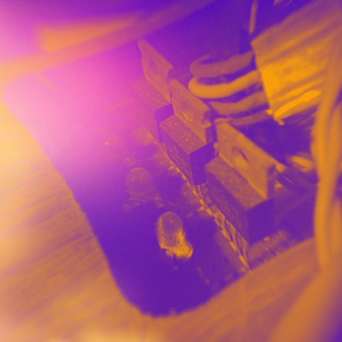 Image Close-up of a small electronic component with metal blocks and coiled wiring, shown in a purple and orange tinted image.